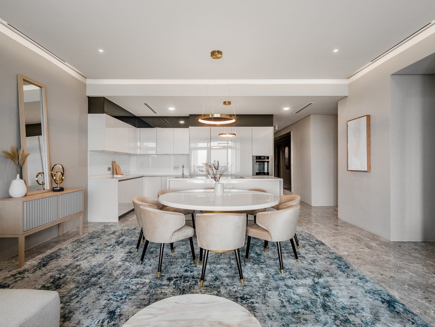 Round dining table with upholstered chairs on a large rug, a floor mirror and a sideboard beside an open kitchen, Four Seasons Place, Kuala Lumpur, Malaysia, by Blaine Robert Design